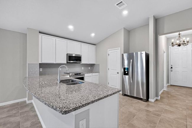 Kitchen with appliances with stainless steel finishes, a peninsula, backsplash, light stone countertops, and white cabinets | Image 15