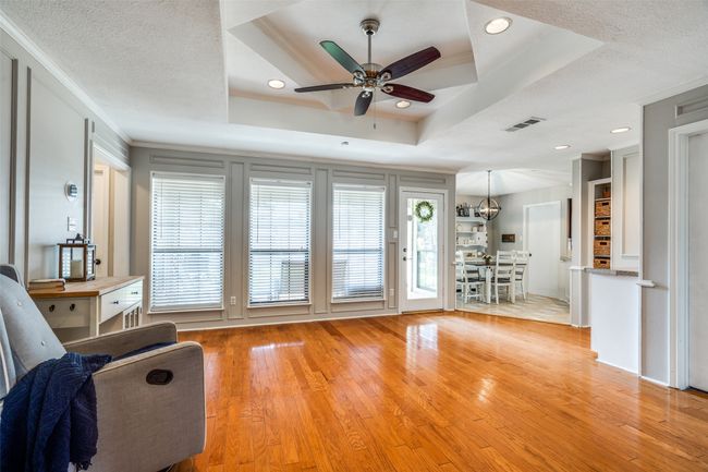Living room featuring ceiling fan, light wood-type flooring, healthy amount of natural light, ornamental molding, and a tray ceiling | Image 9