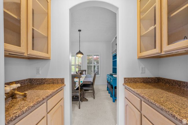 Kitchen featuring arched walkways, light stone counters, glass insert cabinets, light brown cabinets, and light carpet | Image 19