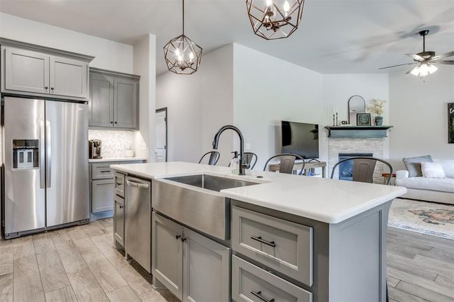 Kitchen with stainless steel appliances, a stone fireplace, gray cabinets, a sink, and open floor plan | Image 35