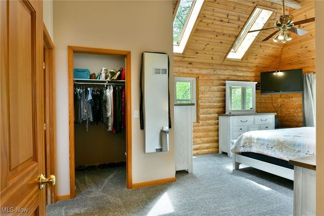 Bedroom featuring high vaulted ceiling, log walls, a walk in closet, baseboards, and carpet floors | Image 23