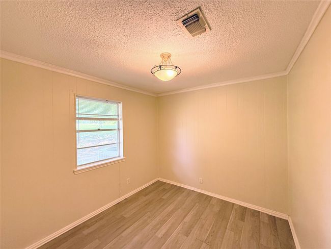 Empty room featuring light wood-style flooring, a textured ceiling, and crown molding | Image 17