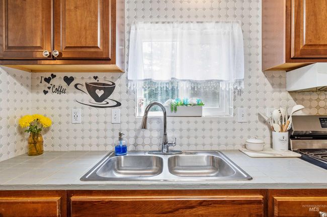 Kitchen with tile countertops, stainless steel gas range, brown cabinetry, and decorative backsplash | Image 8