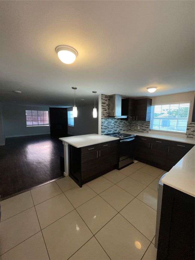 Kitchen with stove, dark cabinets, light countertops, tasteful backsplash, and light tile patterned flooring | Image 4