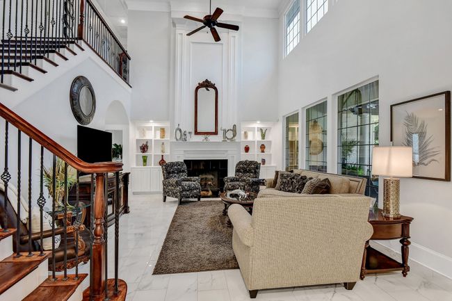 Living room featuring marble look tiles, a towering ceiling, stairs, a ceiling fan, and a fireplace | Image 7