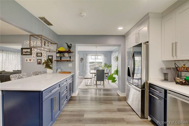 Kitchen with blue cabinetry, hanging light fixtures, stainless steel fridge with ice dispenser, white cabinets, and light wood-type flooring | Image 38