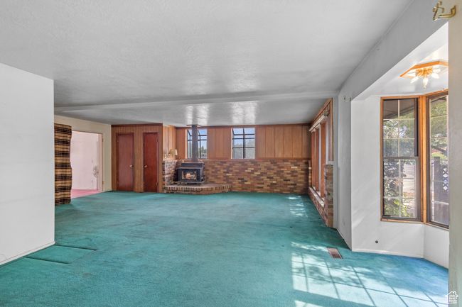 Unfurnished living room featuring carpet floors, a wood stove, and a textured ceiling | Image 6