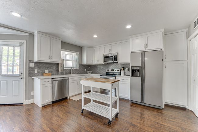 Kitchen featuring recessed lighting, white cabinetry, backsplash, dark wood finished floors, and stainless steel appliances | Image 9