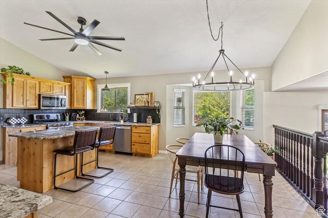 Kitchen featuring stainless steel appliances, vaulted ceiling, decorative backsplash, a kitchen island, and a chandelier | Image 4
