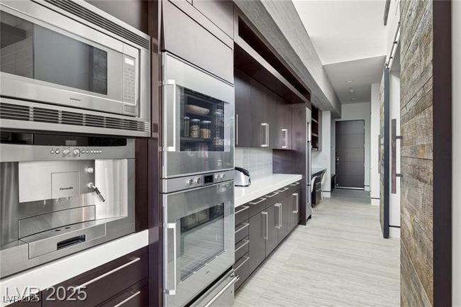 Kitchen featuring modern cabinets, stainless steel appliances, light wood-style floors, decorative backsplash, and dark brown cabinets | Image 22