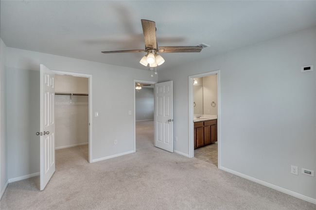 Unfurnished bedroom featuring a walk in closet, baseboards, ceiling fan, light colored carpet, and a closet | Image 30