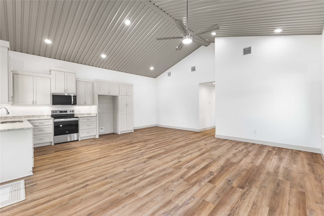 Kitchen with appliances with stainless steel finishes, a sink, a ceiling fan, light stone countertops, and baseboards | Image 10
