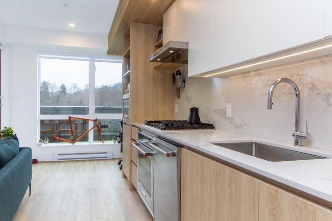 Kitchen with modern cabinets, baseboard heating, appliances with stainless steel finishes, a sink, and light stone countertops | Image 8
