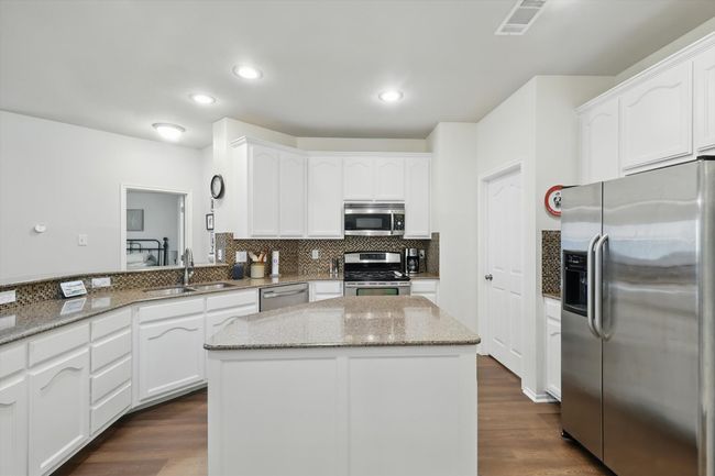 Kitchen featuring stainless steel appliances, white cabinets, light stone counters, backsplash, and dark wood-style flooring | Image 17