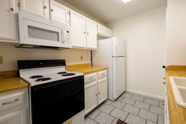 Kitchen featuring white appliances, light countertops, white cabinetry, and light tile patterned flooring | Image 29