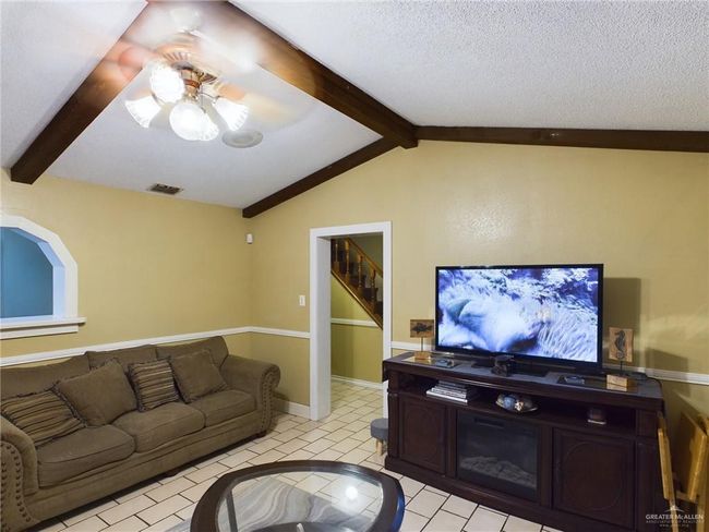 Tiled living room with a textured ceiling, vaulted ceiling with beams, and ceiling fan | Image 5