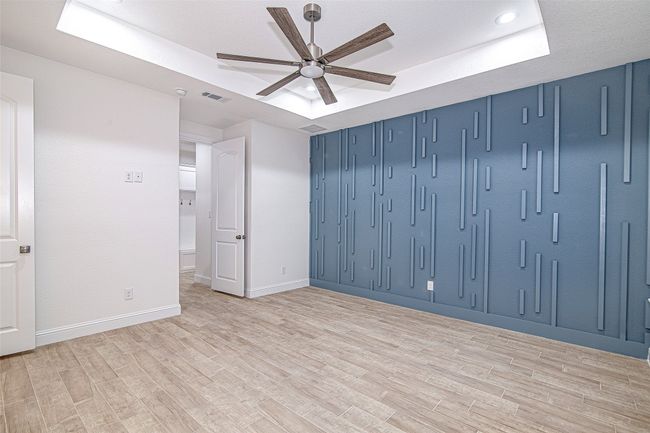 Empty room with a tray ceiling, a ceiling fan, light wood-style floors, baseboards, and recessed lighting | Image 22