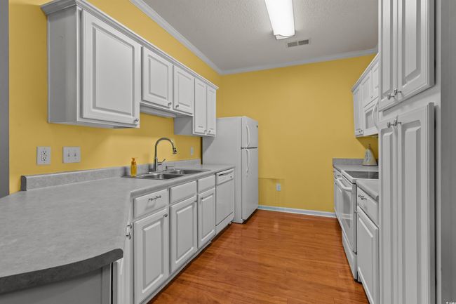 Kitchen with white appliances, ornamental molding, a sink, light wood-style floors, and white cabinetry | Image 12