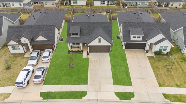 In an aerial view of the front yard, you’ll see a well-maintained expanse of lush green grass, providing a welcoming and open feel. A tree, perhaps near the center or off to the side, adds shade and natural beauty to the landscape. A neatly organized garden, filled with colorful plants or flowers, borders the lawn, adding a touch of vibrancy and charm. The green front door stands out as a focal point, adding a pop of color and inviting entry into the home. The entire yard is carefully designed. | Image 30
