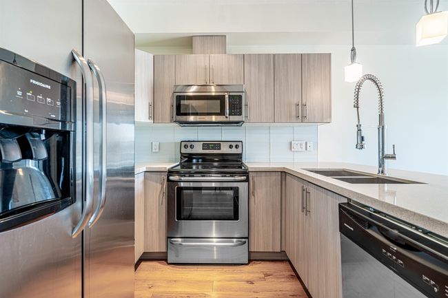 Kitchen featuring stainless steel appliances, decorative backsplash, pendant lighting, light stone countertops, and modern cabinets | Image 10