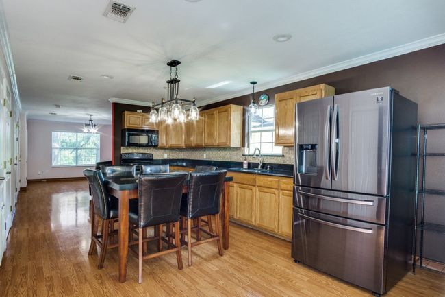 Kitchen featuring black appliances, dark countertops, light wood-style flooring, tasteful backsplash, and a chandelier | Image 12