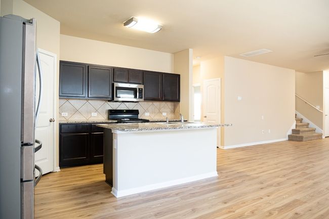 Kitchen featuring stainless steel appliances, light wood-style flooring, decorative backsplash, an island with sink, and a sink | Image 5