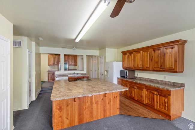 Kitchen featuring dark colored carpet, a center island, black electric cooktop, and brown cabinetry | Image 11