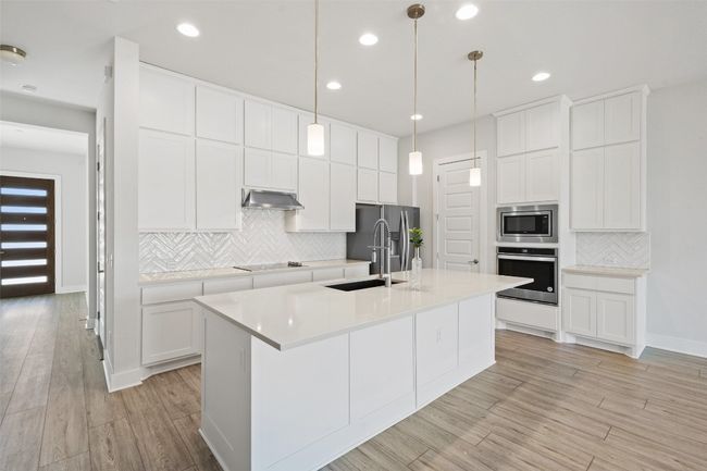 Kitchen with decorative backsplash, stainless steel appliances, light wood-type flooring, a kitchen island with sink, and light countertops | Image 15