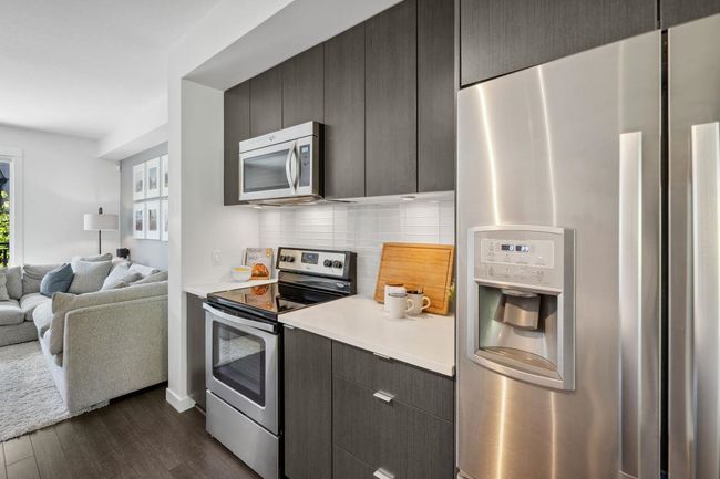 Kitchen with stainless steel appliances, dark wood finished floors, open floor plan, light countertops, and backsplash | Image 12