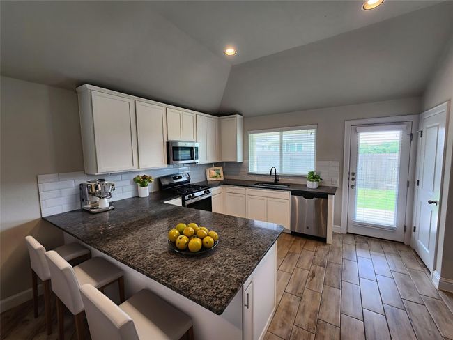 Kitchen with stainless steel appliances, white cabinets, lofted ceiling, backsplash, and a peninsula | Image 7
