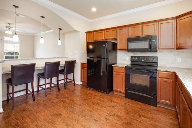 Kitchen featuring dark wood-style floors, decorative backsplash, black appliances, brown cabinetry, and a breakfast bar area | Image 6