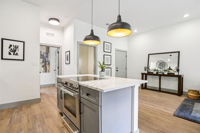 Kitchen with stainless steel range, light stone counters, hanging light fixtures, light wood finished floors, and gray cabinets | Image 9