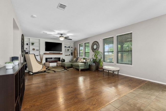 Tiled living area featuring ceiling fan, a glass covered fireplace, and built in shelves | Image 7