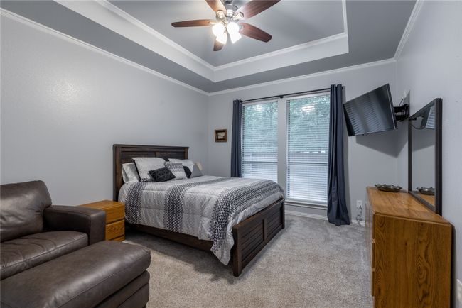 Carpeted bedroom featuring a raised ceiling, ceiling fan, and crown molding | Image 29