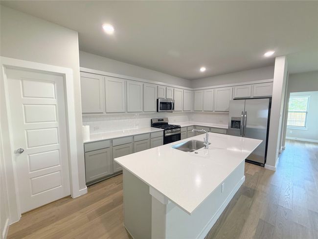 Kitchen with appliances with stainless steel finishes, a sink, gray cabinets, light wood-style flooring, and a kitchen island with sink | Image 12