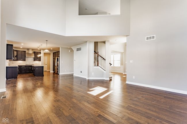 unfurnished living room featuring stairway, dark wood-style flooring, a towering ceiling, and visible vents | Image 16