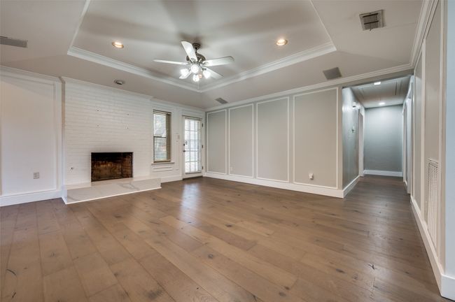 Unfurnished living room featuring attic access, ceiling fan, hardwood / wood-style flooring, ornamental molding, and a fireplace | Image 7