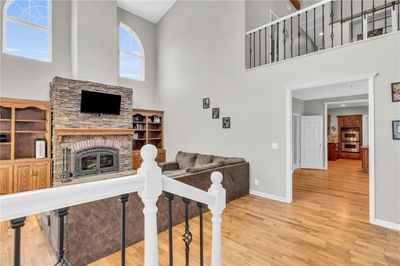 Living room featuring a stone fireplace, light hardwood / wood-style floors, a healthy amount of sunlight, and a high ceiling | Image 3