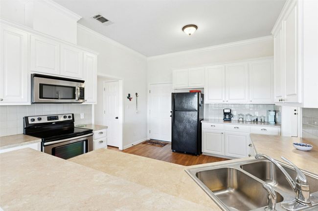 Kitchen with appliances with stainless steel finishes, light countertops, white cabinetry, ornamental molding, and decorative backsplash | Image 10