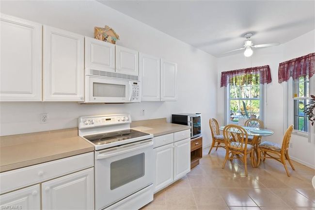 Kitchen with white cabinets, ceiling fan, white appliances, and light tile floors | Image 14