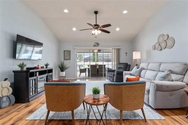 Living area with volume ceilings and lighted ceiling fan opens to lanai and patio area. Furnishings including electric fireplace and wall mounted TV are optional. | Image 11