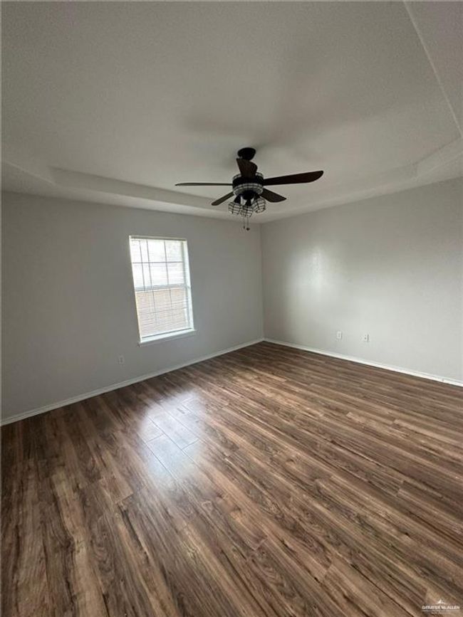 Spare room featuring dark wood-type flooring, a ceiling fan, baseboards, and a tray ceiling | Image 8