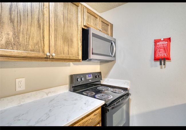 Kitchen with stainless steel microwave, black range with electric cooktop, light countertops, and brown cabinetry | Image 18