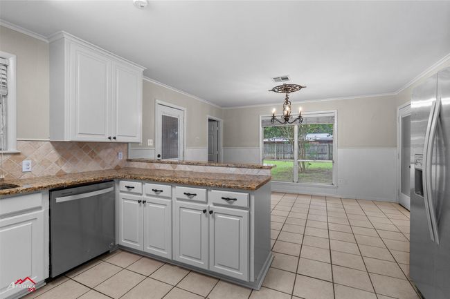 Kitchen with stainless steel appliances, light tile patterned floors, white cabinets, a chandelier, and wainscoting | Image 7