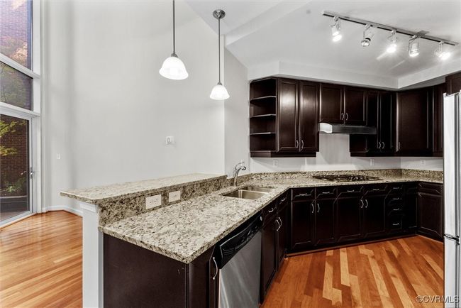Kitchen with stainless steel appliances, a peninsula, a sink, light wood-style floors, and under cabinet range hood | Image 8