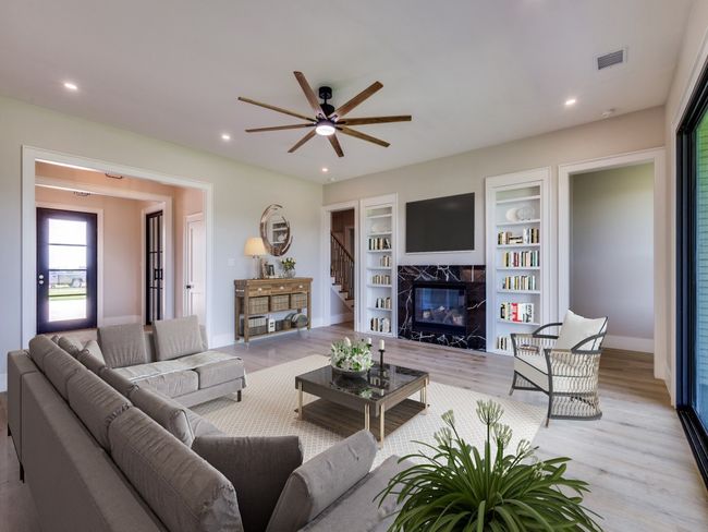 Virtual Staged Living room featuring light wood flooring, a marble surround fireplace, ceiling fan, baseboards, and recessed lighting, built in bookcases with hidden storage, triple pane sliding glass doors for access to covered patio | Image 16