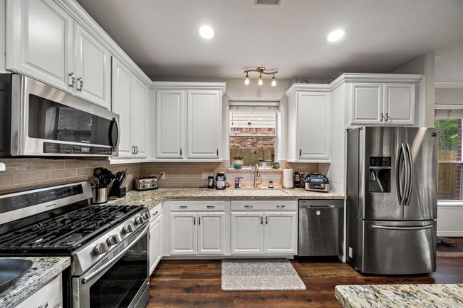 This modern kitchen features stainless steel appliances, white cabinetry with soft close doors, and granite countertops. It has a gas stove and a built-in microwave. The space is well-lit with recessed lighting and a window above the sink, providing a bright and inviting atmosphere. | Image 6