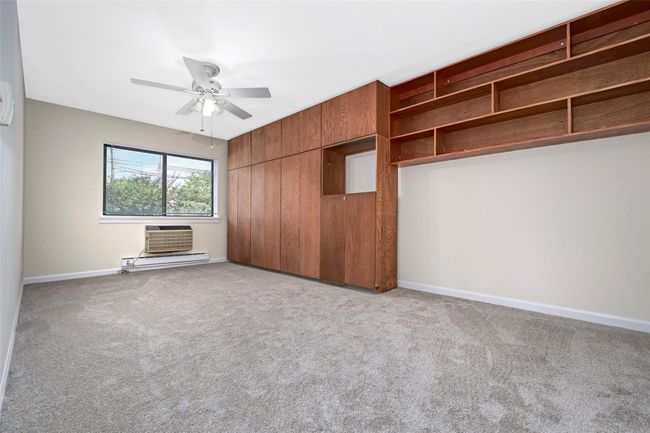 Primary bedroom featuring new carpeting, baseboard heating, a wall mounted air conditioner, and a large walk in closet | Image 12