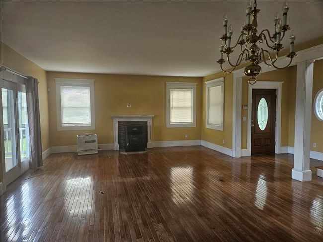 Unfurnished living/dining room featuring ornate columns, a notable chandelier, and hardwood / wood-style floors | Image 7