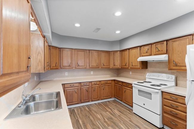This kitchen features ample wooden cabinetry, a dual-basin sink, and an electric stove. It has a neutral countertop and backsplash, offering a spacious and functional cooking area. | Image 17